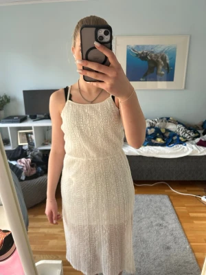 Vit stickad klänning med slits - Säljer en vit klänning med spets och slits på sidan då den ktne andvända och är för liten. Klänningen har ett ganska tydligt men fint mönster. Perfekt för sommar dagar elelr när det bara är varmt ute.