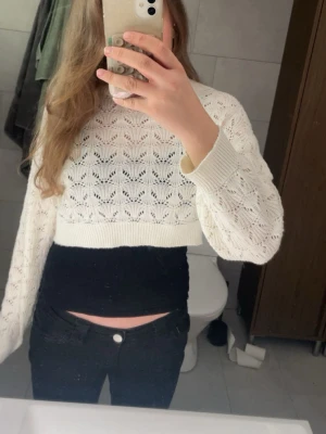 Vit cropped stickad tröja - Säljer en vit cropped stickad tröja med hålmönster och långa ärmar. Tröjan har ribbade muddar vid ärmslut och nederkant, och ett snyggt, luftigt mönster.
