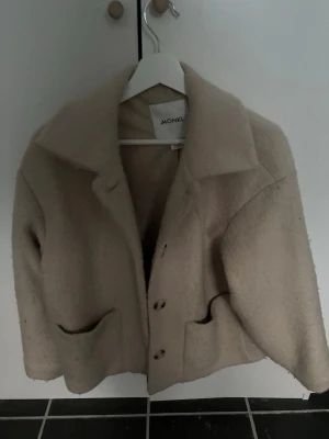 Beige vårjacka från Monki - Snygg beige cardiganjacka från Monki i ullblandning. Jackan har stora slag, knäppning framtill med tre knappar och två rymliga fickor. 