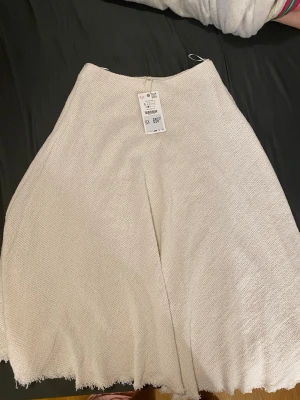 Vit långkjol i strukturerat tyg - Säljer en vit långkjol med rå kant och strukturerat tyg. Kjolen har en enkel och clean look med lätt utställd form. Perfekt för dig som gillar minimalistisk stil och vill ha något som sticker ut utan att vara för mycket.