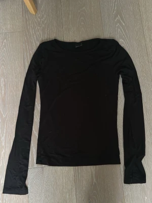Svart långärmad tröja  - En stilren svart långärmad topp med rund halsringning. Toppen har en slim passform och är tillverkad i ett mjukt och stretchigt material, perfekt att matcha med jeans eller kjol. Enkel och tidlös design som funkar till många olika looks.