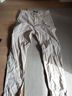 Beige linnebyxor från 157 - Snygga beige linnebyxor från 157 i storlek S. Byxorna har rak passform, knapp och dragkedja framtill samt klassiska fickor. Perfekta för en avslappnad och trendig stil. Tillverkade i ett lätt och luftigt linnematerial.
