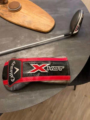 Callaway X Hot driver - Säljer en Callaway X Hot golfklubba med huvskydd. Klubban har svart, silver och röda detaljer och är tillverkad i metall och kompositmaterial. Perfekt för dig som vill ha en kraftfull driver till golfbanan.
