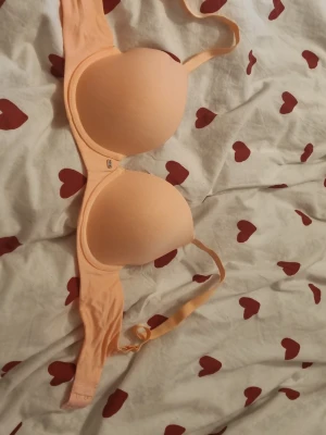 Ljus persikofärgad push-up bh - Säljer en ljus persikofärgad push-up bh med släta kupor och justerbara axelband. Bh:n har bygel och breda sidopartier för extra stöd. Perfekt för dig som vill ha en enkel och stilren bh under dina kläder.