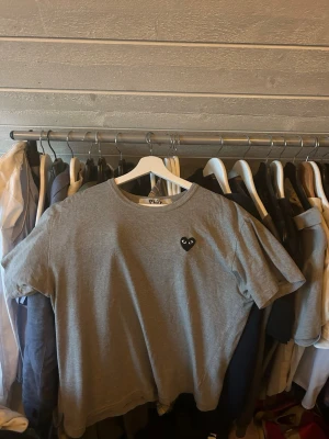 Grå t-shirt från Comme des Garçons Play - Säljer en grå t-shirt från Comme des Garçons Play med det ikoniska svarta hjärtat på bröstet. T-shirten har rund hals och korta ärmar, perfekt för en chill och stilren look. Materialet är mjuk bomull som känns skönt mot huden. Storleken är XL men passar M/L