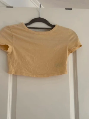 Gul croppad topp från Divided - Snygg croppad topp i ljusgul färg från Divided. T-shirten har rund halsringning och korta ärmar. Perfekt till jeans eller kjol för en avslappnad look.