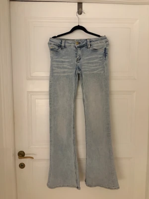 Ljusblå bootcut jeans från cheap Monday  - Snygga ljusblå jeans från cheap Monday med bootcut passform och låg midja. Jeansen har klassiska fem fickor, slitningar framtill och en cool patch på baksidan. Perfekta för dig som gillar retrostil och vill sticka ut.