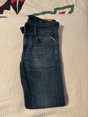Blå jeans från Replay med slitningar - Snygga blå jeans från Replay med klassisk femficksdesign och diskreta slitningar framtill. Jeansen har en smal passform och detaljerad söm vid fickorna. Perfekta för en trendig och avslappnad look. W27 L30🙌 Vill ni ha mer bilder eller några andra frågor är det bara att höra av sig! 