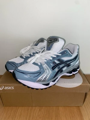 Asics Gel Kayano 14 - Snygga Asics Gel Kayano 14 i färgen White/Fjord Grey. Nya med prislapp, säljer pga att de var för små för mig. Storlek 42 och slutsålda på de flesta hemsidor i denna färg!