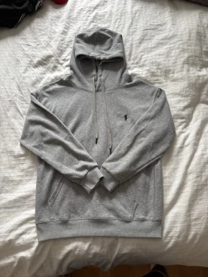 Grå hoodie från Polo Ralph Lauren - Snygg grå hoodie från Polo Ralph Lauren med klassisk huva och dragsko. Tröjan har en broderad logga på bröstet och en stor magficka. Tillverkad i mjukt bomullsmaterial och har ribbade muddar vid ärmslut och nederkant. Perfekt för en chill och stilren look. Nästan inte använd någonting och inga hål eller fläckar mm. Storlek M passar S. Bara att höra av sig vid någon fundering🙌 Pris kan diskuteras🤝