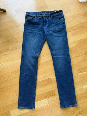 Blå slim fit jeans från BOSS - Snygga blå slim fit jeans från BOSS med klassisk femficksdesign. Jeansen har normal midja, raka ben och är tillverkade i stretchigt denim för extra komfort. Perfekta för en avslappnad och trendig look. Aldrig använda. 