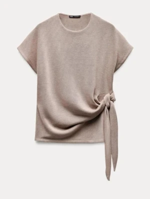 Beige topp med knyt från Zara - Stilren beige topp från Zara med korta ärmar och snygg knytdetalj i sidan. Toppen har rund halsringning och är tillverkad i ett mjukt material som ger en avslappnad men trendig look.