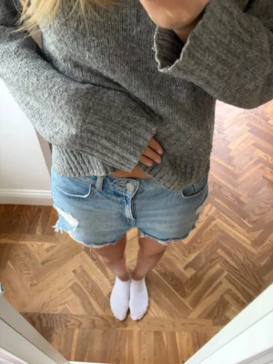 Ljusblå denimshorts med slitningar - Säljer ett par ljusblå denimshorts med råa kanter och slitna detaljer framtill. Klassisk femficksmodell med knapp och dragkedja. Perfekta för varma dagar och enkel att matcha med allt.
