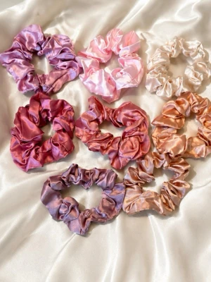 Satin scrunchies i pastellfärger - Säljer ett set med åtta scrunchies i glansigt satinmaterial. Färgerna är blandade i pastelliga toner av rosa, lila, persika och beige. Perfekta för att ge en mjuk och lyxig känsla till din frisyr. Snygga att ha både i håret och runt handleden. Dem kostar 15kr/styck. Skriv i privat för färg