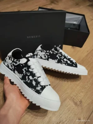 Svarta och vita sneakers från Numeris - Säljer ett par snygga sneakers från Numeris med svart och vit splatter-design. Skorna har chunky vit sula med räfflad undersida, vita snören och tåhätta i vitt. Perfekta för dig som vill sticka ut med en unik look. Materialet är textil och syntet.