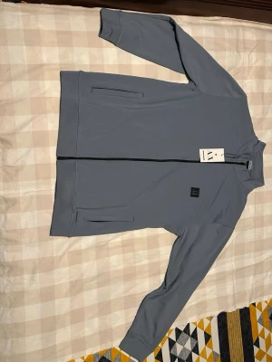 Ljusblå tracksuit från Armani Exchange - Snygg ljusblå hoodie från Armani Exchange med dragkedja framtill och två sidofickor. Minimalistisk design med svart logopatch på bröstet och hög krage. Tillverkad i mjukt material som känns skönt mot huden. Perfekt för en clean och modern look.