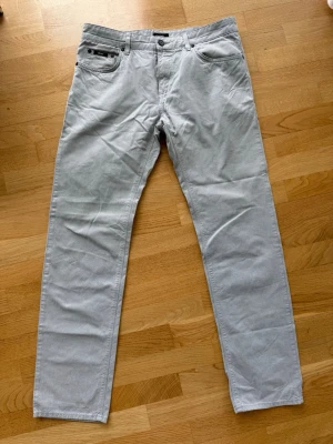Ljusgrå byxa i jeansmodell från  BOSS - Snygga ljusgrå jeansbyxor från BOSS med klassisk femficksdesign och raka ben. Jeansen har diskreta svarta detaljer vid fickorna och är tillverkade i ett mjukt bomullsmaterial. Perfekta för en stilren och avslappnad look.