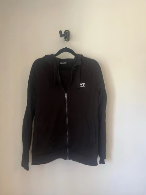 Svart EA7 hoodie, byxor  - Svart hoodie, byx set från EA7 med dragkedja framtill och vit EA7-logga på bröstet. Mjukisbyxor med vit logga på ena benet. Storlek S på båda. Kan köpas enskilt 300 för hoodien, 200 för byxorna 400 för båda. Skick: 7/10 på båda