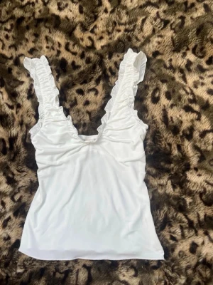 Vit linnetopp med volangaxelband - Supersöt vit linnetopp med djup v-ringning och volangprydda axelband. Toppen har en feminin och fräsch look, perfekt till jeans eller kjol. Materialet känns mjukt och stretchigt mot huden. Helt ny med prislapp 