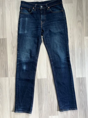 Levis 511 - Säljer ett par mycket fina Levi’s 511 i en snygg mörkblå tvätt med naturligt slitna detaljer. 511:an är den perfekta "slim fit"-modellen – smal utan att vara för tight, vilket ger en modern och stilren siluett.  Mått (platt liggande): • Midja: 41 cm • Innerben: 84 cm • Ytterben: 108 cm • Lår: 26 cm • Benöppning: 17 cm