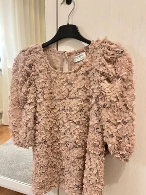 Blommig spetsblus Lindex - Supersöt blus i puderrosa från Lindex med 3D-blommor och spetsdetaljer. Rund halsringning och puffiga trekvartsärmar ger en trendig look. Perfekt för dig som vill sticka ut med en romantisk vibe.