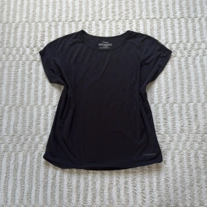 Svart sportig t-shirt från Newbody - Svart t-shirt från Newbody i mjuk och stretchig polyesterblandning. Modellen är enkel med rund hals och korta ärmar, perfekt för träning. Materialet är lätt och andas, vilket gör den skön att ha på sig när du är aktiv. 
