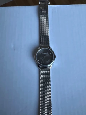 Silverfärgad klocka från Calvin Klein - Stilren klocka från Calvin Klein i silver med mesharmband och rund urtavla. Klockan har minimalistisk design och är tillverkad i metall. Perfekt accessoar för dig som gillar en clean och modern look.