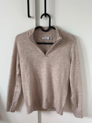 Beige stickad halvzip från kidsbrandstore  - Snygg beige stickad tröja från kidsbrandstore med halvzip och hög krage. Tröjan har långa ärmar och ribbade muddar vid ärmslut och nederkant. Perfekt för lager på lager och enkel att matcha med olika outfits.