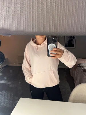 Ljusrosa hoodie med ficka framtill - Säljer en ljusrosa hoodie med huva och stor magficka. Hoodien har en avslappnad passform och ribbade muddar vid ärmarna. Perfekt för dig som gillar en enkel och clean stil. Materialet känns mjukt och bekvämt mot huden.