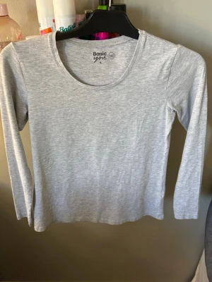 Ljusgrå långärmad topp Basic You - En enkel och stilren ljusgrå långärmad topp från Basic You i mjuk ekologisk bomull. Perfekt basplagg med rund halsringning och normal passform. Superbekväm och lätt att matcha med allt i garderoben.