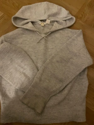 Ljusgrå hoodie från Gina Tricot - Mysig ljusgrå hoodie från Gina Tricot med huva och ribbade muddar vid ärmslut och nederkant. Tillverkad i ett mjukt stickat material som passar perfekt för en avslappnad stil. Enkel och stilren design utan tryck eller dragkedja.