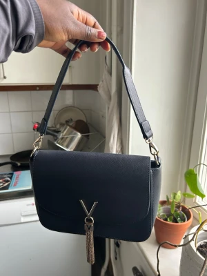 Svart handväska med gulddetaljer - Stilren v mörkblå valentino handväska med justerbart axelband. 