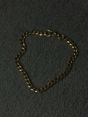 Guld Cubansk Armband 21cm 5mm i Rostfritt Stål - Stilrent cubanskt armband i guldton. Tillverkat i rostfritt stål som är slitstarkt och motståndskraftigt mot rost och missfärgning. En clean men tydlig accessoar som funkar både till vardag och fest, och kan bäras ensam eller tillsammans med andra smycken. 5mm tjocklek ger en balanserad och elegant look på handleden.