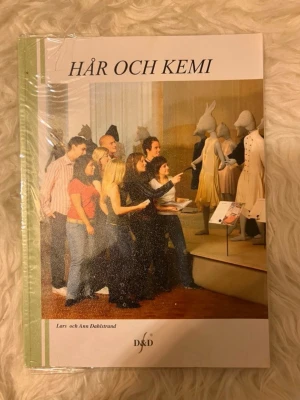 Hår och Kemi kursbok - Kurslitteratur med titeln 'Hår och Kemi' av Lars och Ann Dahlstrand. Boken har ett omslag med gröna och vita färger samt en bild på personer i museum. Innehåller teori om hår, hud och kemiska processer inom frisörutbildning.