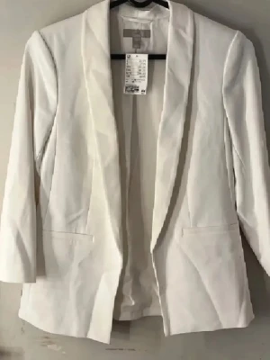 Vit kavaj  - Stilren vit kavaj från H&M med sjalkrage och två fickor framtill. Kavajen har en rak passform och är tillverkad i ett slätt tyg som ger en elegant look. Perfekt för att lyfta vilken outfit som helst. Helt ny oanvänd med prislapp kvar! Vet inte varför bilderna blev så suddiga men det är iallafall en vit och väldigt basic kavaj:)