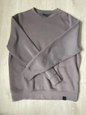 Grå sweatshirt från Pull&Bear - En stilren grå sweatshirt från Pull&Bear i storlek S. Tröjan har rund halsringning, långa ärmar och ribbade muddar vid ärmslut och nederkant. Perfekt för en avslappnad look och enkel att matcha med jeans eller joggers.