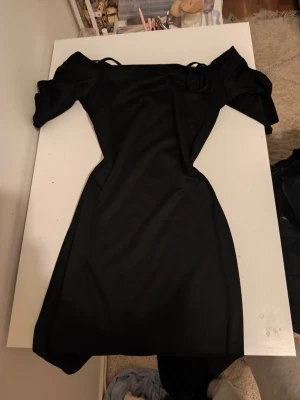 Svart offshoulder kort klänning - Snygg svart kort klänning med offshoulder-design och puffiga ärmar. Klänningen har en figurnära passform och är perfekt för dig som vill ha en stilren och trendig look. Tillverkad i ett mjukt och stretchigt material som sitter bekvämt.