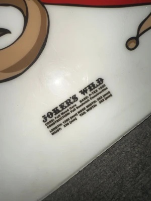 Joker's Wild snowboard med bindningar - Snowboard från Joker's Wild med färgglad joker-grafik och svarta bindningar. Brädan har vit bas med illustration av en joker som håller spelkort. Konstruktion i träkärna och sandwich-teknik. Mått: längd 126 cm. Pris kan diskuteras men start priset är 400 kr.