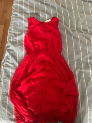Röd ärmlös kortklänning - Snygg röd kortklänning med markerad midja och ärmlös design. S.13-14