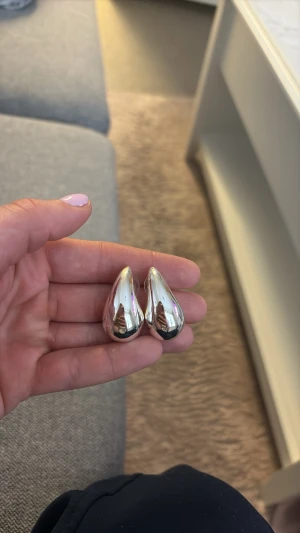 Silvriga droppformade örhängen från Snö of Sweden - Säljer ett par coola, droppformade örhängen i blankt silverfärg. De har en modern och minimalistisk look som verkligen sticker ut. Perfekta för dig som gillar statement-smycken och vill ha något unikt i smyckeslådan. I äkta silver från snö of Sweden. Använd ett fåtal gånger