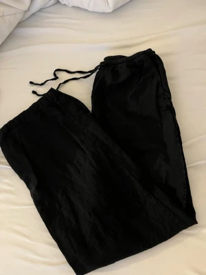 Svarta linnebyxor med dragsko - Är 171 cm. Ett par svarta linnebyxor med avslappnad passform och dragsko i midjan. Byxorna har raka ben och är tillverkade i ett mjukt och bekvämt material, perfekta för chill dagar hemma eller när du vill vara extra comfy. 
