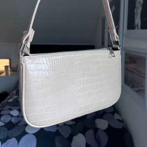 Beige axelväska med krokodilmönster - Snygg beige axelväska med krokodilmönster och dragkedja. Perfekt för att ge din outfit en stilren touch. Väskan har en justerbar axelrem, ett stort rymligt fack och tre mindre 🤍Storlek: 27x16cm
