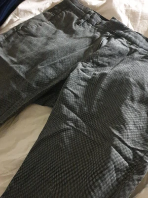 Gråsmåmönstrade kostymbyxor - Snygga grå kostymbyxor med diskret småmönstrad struktur. Klassisk rak passform med bälteshällor och sidfickor. Perfekta för en stilren look. Materialet känns lätt och passar året runt.