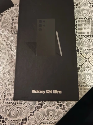 Samsung Galaxy S24 Ultra svart - Snygg Samsung Galaxy S24 Ultra i svart med stilren design och flera kameror på baksidan. Telefonen har en matt finish och levereras i originalförpackning. Perfekt för dig som vill ha en kraftfull Android-mobil med stor skärm och S Pen. Mobilskal med köpet