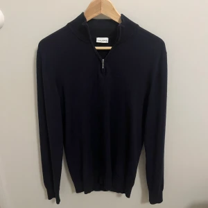 Mörkblå halvzip från John Henric  - Snygg mörkblå stickad halvzip från John Henric. Storlek M. Perfekt för lager på lager och enkel att matcha med olika outfits. Har en lagning på bröstet men det syns knappt när man har den på. 