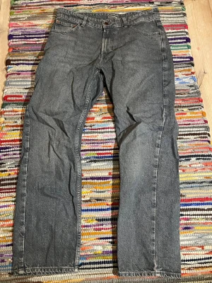 Grå raka jeans med fem fickor - Ett par klassiska grå jeans med rak passform och fem fickor i storlek W32 och L30 Jeansen har bälteshällor, knappgylf och subtila slitningar för en avslappnad look. Tillverkade i denim med en tidlös vibe som passar till det mesta.