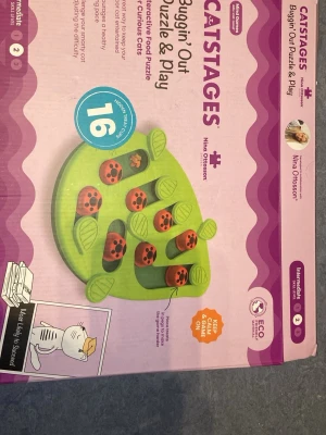 Catstages Buggin' Out kattpussel - Interaktivt matpussel för katter från Catstages, designat av Nina Ottosson. Pusslet är grönt med röda nyckelpigor och bladformade delar i plast. Perfekt för att aktivera nyfikna katter och gömma godis eller torrfoder. Innehåller 16 olika gömställen.