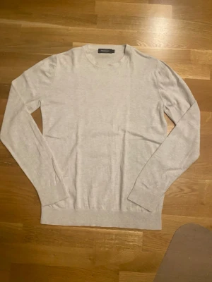 Ljusgrå tröja från Dressmann - En stilren beige tröja från Dressmann med rund halsringning och långa ärmar. Tröjan är tunnstickad och har en klassisk passform. 