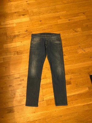 Blå Replay Anbass jeans - Säljer ett par blå jeans från Replay, modell Anbass. Jeansen har en klassisk femficksdesign, smal passform och snygga slitningar på låren. Materialet är mjukt denim med stretch för extra komfort. Perfekta för en avslappnad och trendig look.
