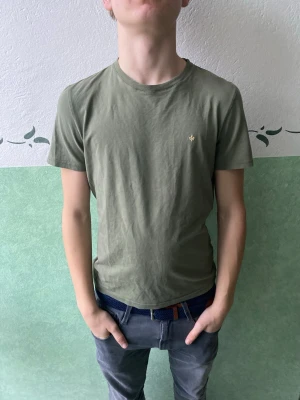 Olivgrön t-shirt med liten logga - Snygg olivgrön t-shirt med rund hals och korta ärmar. Liten diskret logga i guld på bröstet. Enkel och stilren design som passar till det mesta. Tillverkad i mjukt material för skön känsla.